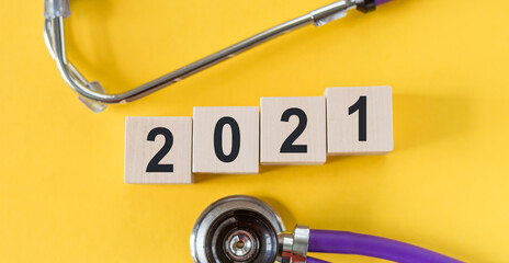 Wooden cubes with numbers 2021 and a stethoscope on a yellow background. Medical expectation 2021 concept.