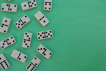 Deck of scattered dominoes on vibrant green background. Top down view flat lay with empty space for text