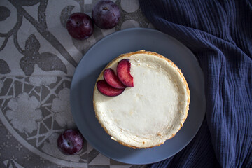Homemade cheesecake decorated with red plums. Top view photo on grey background with copy space.  
