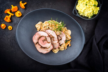 Traditional French barbecue lamb roast sliced with chanterelles in cream sauce and mashed potatoes offered as top view on a design cast-iron plate