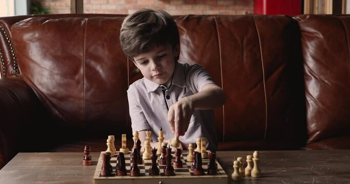 Pensive little 6s boy sitting at home on couch makes move plays chess. Game help develop abstract thinking, raise IQ, improves memory and concentration of kid. Skills and educational leisure concept