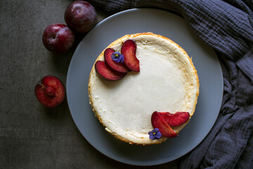 Homemade cheesecake decorated with red plums. Top view photo on grey background with copy space.  
