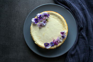 Homemade cheesecake decorated with blue wild pansy flowers. Top view photo on grey background with copy space.  

