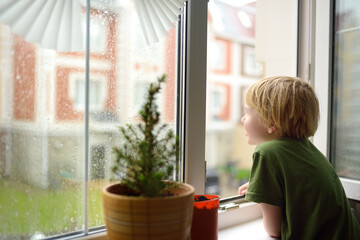 Little boy watching the rain outside at opened window. Bad weather - wind and downpour. Child waiting of rainfall finish. Inquisitive kid explore nature.