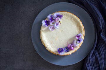 Homemade cheesecake decorated with blue wild pansy flowers. Top view photo on grey background with copy space.  
