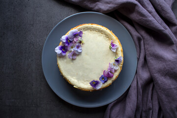 Homemade cheesecake decorated with blue wild pansy flowers. Top view photo on grey background with copy space.  
