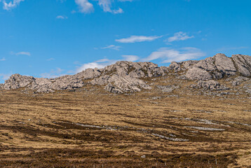 Falkland Islands, UK - December 15, 2008: Wide windswept bare sloping landscape of dry land with gray sharp rocky outcrop under blue cloudscape.