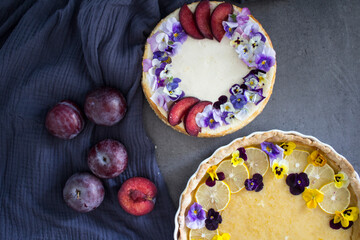 Homemade sweet cakes on a table. Close up photo of lemon tart, cheesecake decorated with flowers and fresh citrus fruits on grey background. Colorful sweet food. 
