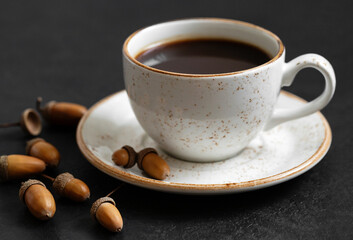 Black coffee in a white cup and acorns. Acorn coffee on a black background. The concept of a caffeine substitute
