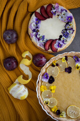 Cheesecake and lemon tart on a table. Two dessert pies decorated with edible flowers. 
