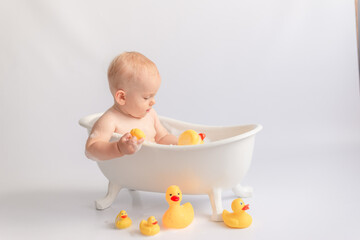 small child bathes in a white tub with rubber ducks and foam