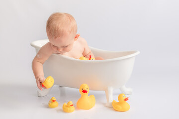 ittle kid likes to swim in a white tub with rubber ducks and foam