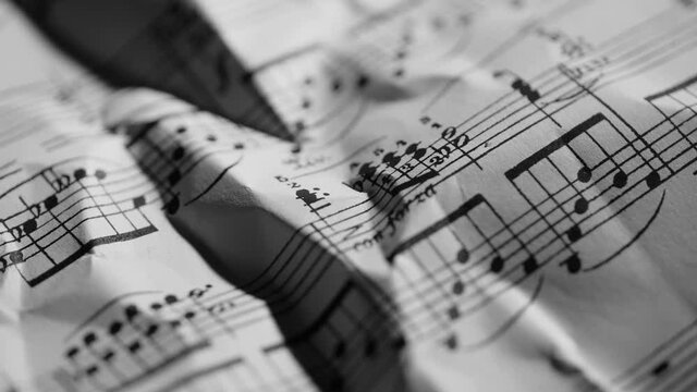 4K Close up of sheet music of a classical piece. Rotating macro video of a paper with notations for piano with elegant shadows and highlights. Artistic and textured background.