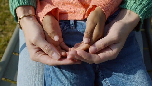 Close up of caucasian mother holding hands of little african child sitting outdoors