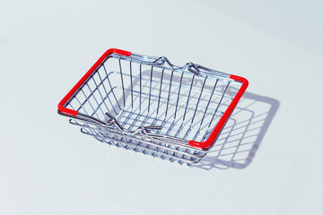 Empty metal shopping basket with red handles on grey background. Living wage. Hard shadows.