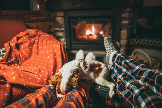 Unrecognizable Couple Feet In Woollen Socks Relax By Cozy Burning Fireplace With Cute Puppy Sleeping By. Snug evening by the warm fire during Christmas season in Switzerland Alps Mountain Chalet