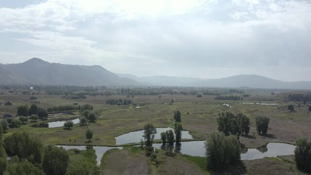 Serene Landscape Scenery in Wyoming Tetons, Green Valley With Ponds and Meadows Outside of Jackson City, Cloudy Summer Day, Cinematic Drone Aerial View tracking sideways in country side