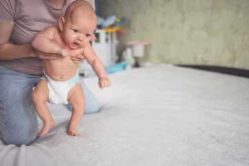 Mom doing exercises for baby in diaper. Cute emotional funny newborn boy learns to walk.