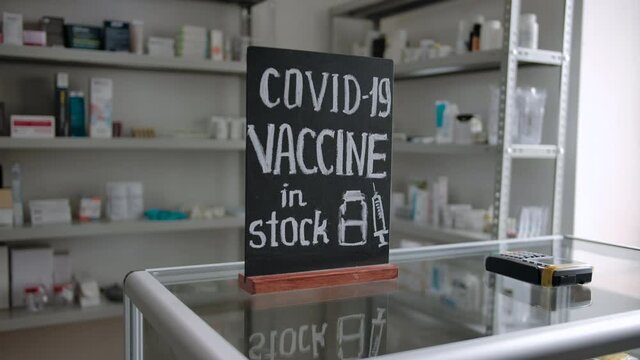COVID-19 vaccine in stock inscription on a chalkboard at a pharmacy. Dolly in shot indoor of modern drugstore interior. Shelfs with medicines, computer display and keyboard, terminal for payment.