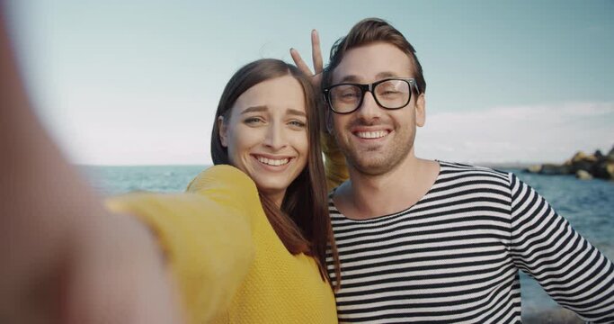 Close-up of happy young couple grimacing while holding the camera and making funny photo against the background of sea.