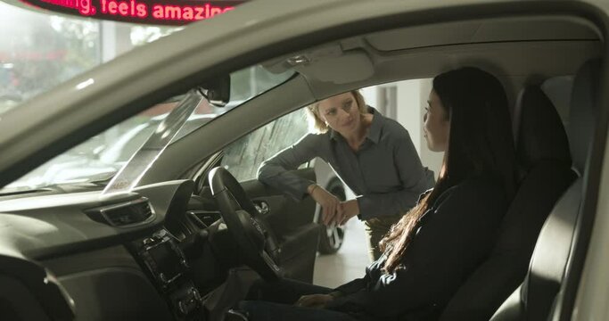 Female test driving new electric car in automotive showroom, saleswoman advising