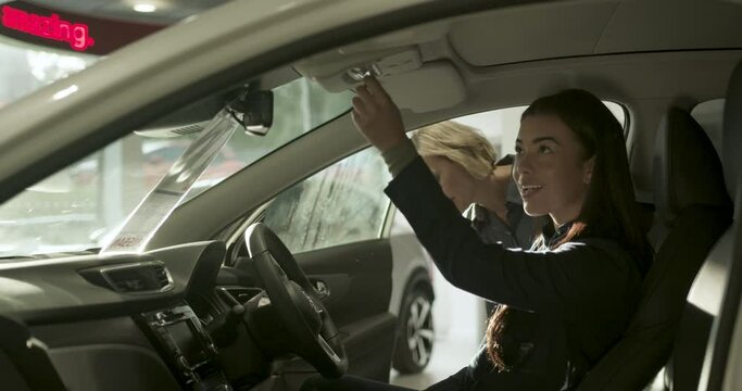 Female test driving new electric car in automotive showroom, saleswoman advising