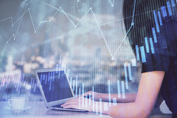 Double exposure of businesswoman hands typing on computer and forex chart hologram drawing....
