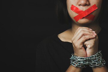 Asian woman blindfold wrapping mouth with red adhesive tape and she was hand tethered on black background. Freedom speech censorship and stop talk, International Human Right day - obrazy, fototapety, plakaty