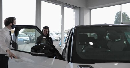 Car salesman showing customer car in automotive dealership showroom