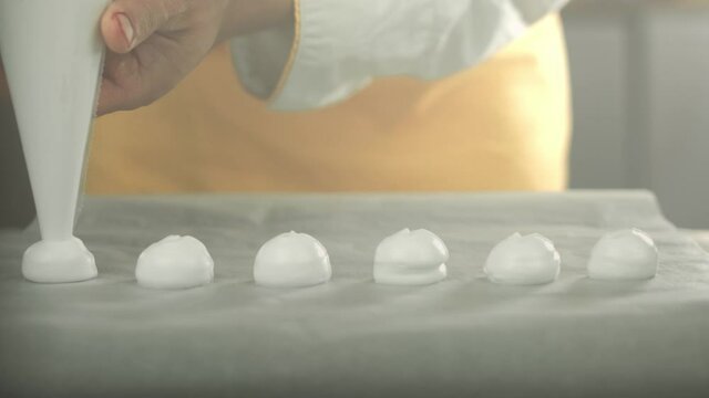 Chef places whipped egg white cream with a piping bag on a backing plate to make meringue. Shot in 4K. Shallow depth of field.