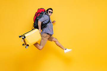 Travel portrait of Young excited Caucasian male tourist with baggage jumping in mid-air in isolated studio yellow background