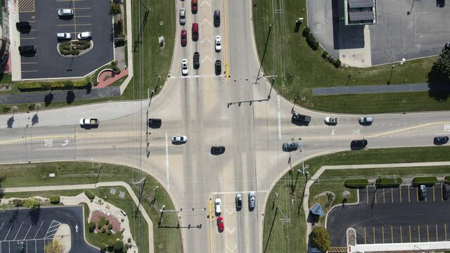 Static aerial establishing shot of intersection in the American suburbs. Traffic signal light, cars stopped at light, traffic drives on road, drone above cars.
