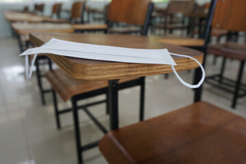 Medical face mask for protecting anti-bacteria anti-virus and Coronavirus Disease COVID-19 on wood lecture chairs in the empty classroom on blurred background. Back to school concept.