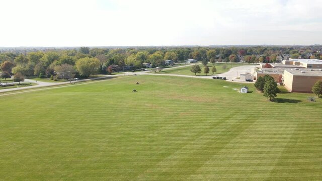 Slowly flying over of various school or
 community fields in a lawn mowing process. American suburban neighborhood

