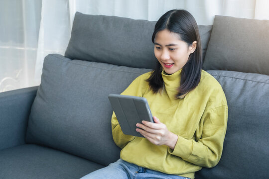 Beautiful Asian happy smile woman using tablet technology playing entertainment internet browsing social media website studying business, in free time domestic home lifestyle comfy in living room