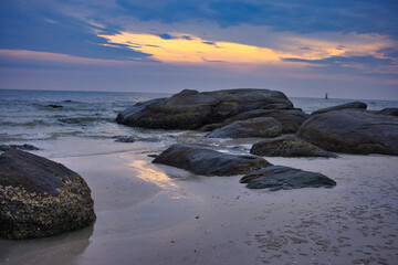 Fototapeta na wymiar This unique photo shows the sunrise on Hua Hin Beach. You can see the first rays of the sun through the clouds and the big rocks on the beach
