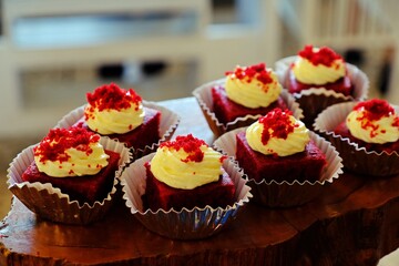 Delicious homemade red velvet cake with cream cheese frosting topping with red sprinkles ready to serve on wooden tray.