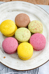 Multicolored macarons on a plate and wooden background