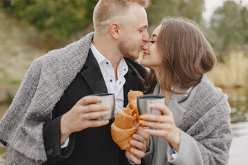 Cute couple in a park. Lady in a gray coat. People with a thermos and croissant.