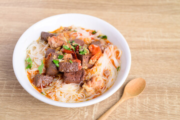 Northern Thai food (Kanom Jeen Nam Ngeaw), Rice noodles spicy soup with pork and pork blood in a bowl with spoon on wooden background