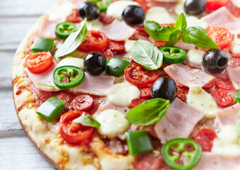 Pizza with ham, mozzarella cheese, cherry tomatoes, green and jalapeno pepper, black olives and fresh basil. Bright background. Close up.	