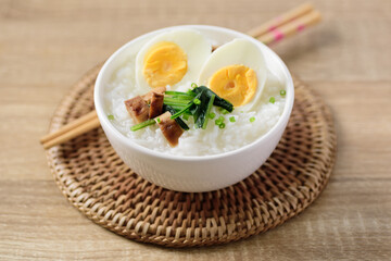 Asian food, Rice soup with boiled egg, grilled mushroom and spinach in a bowl on woven rattan sheet