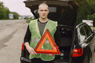 Driver putting warning triangle on asphalt road. Emergency stop concept.