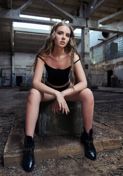Beautiful girl dressed in black panties and shirt sitting in forsaken factory and smoking cigarette. Portrait of pretty young woman in industrial place