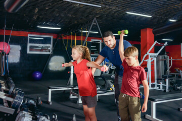 A young and sports coach is engaged with children in the gym.