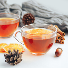 Hot spicy autumn or winter tea with lemon, cinnamon and pine cones on white table and gray cozy sweater