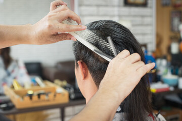 Asian young man being cut from long hair to short hair with scissor by professional barber in...