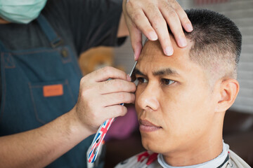 Asian young man being haircut with razor by professional barber in barbershop.