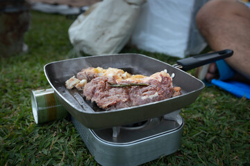 Close up on woman grilled pork barbecue in the picnic pan and cooking food for friend and family while camping with family in the camping site.