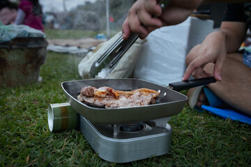 Close up on woman grilled pork barbecue in the picnic pan and cooking food for friend and family while camping with family in the camping site.